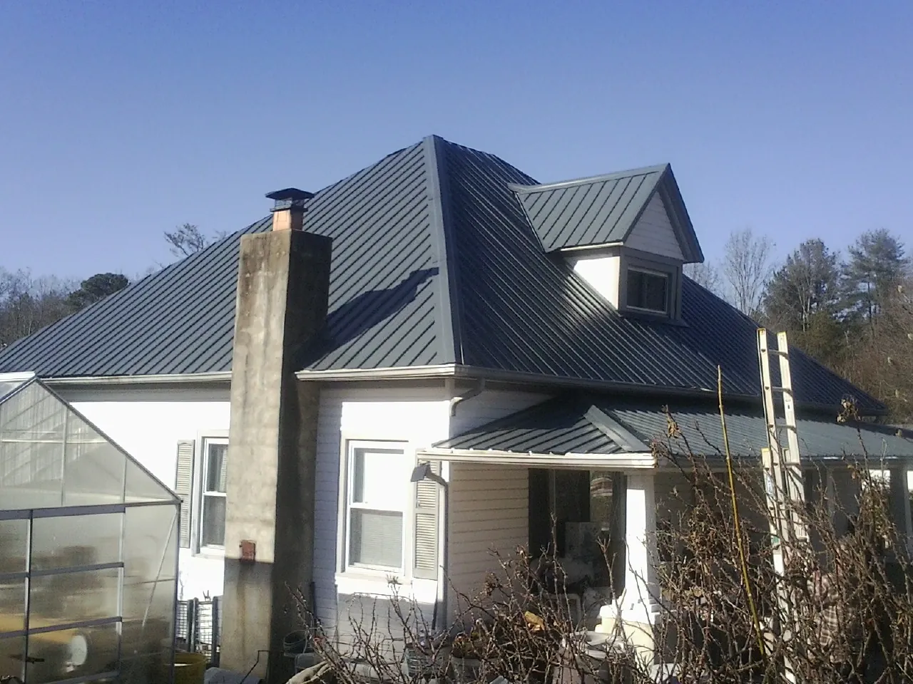Dark blue standing seam metal roof on a white farmhouse with dormer — Slate & Tile Roof Repair by Roofing Brothers in Vanleer