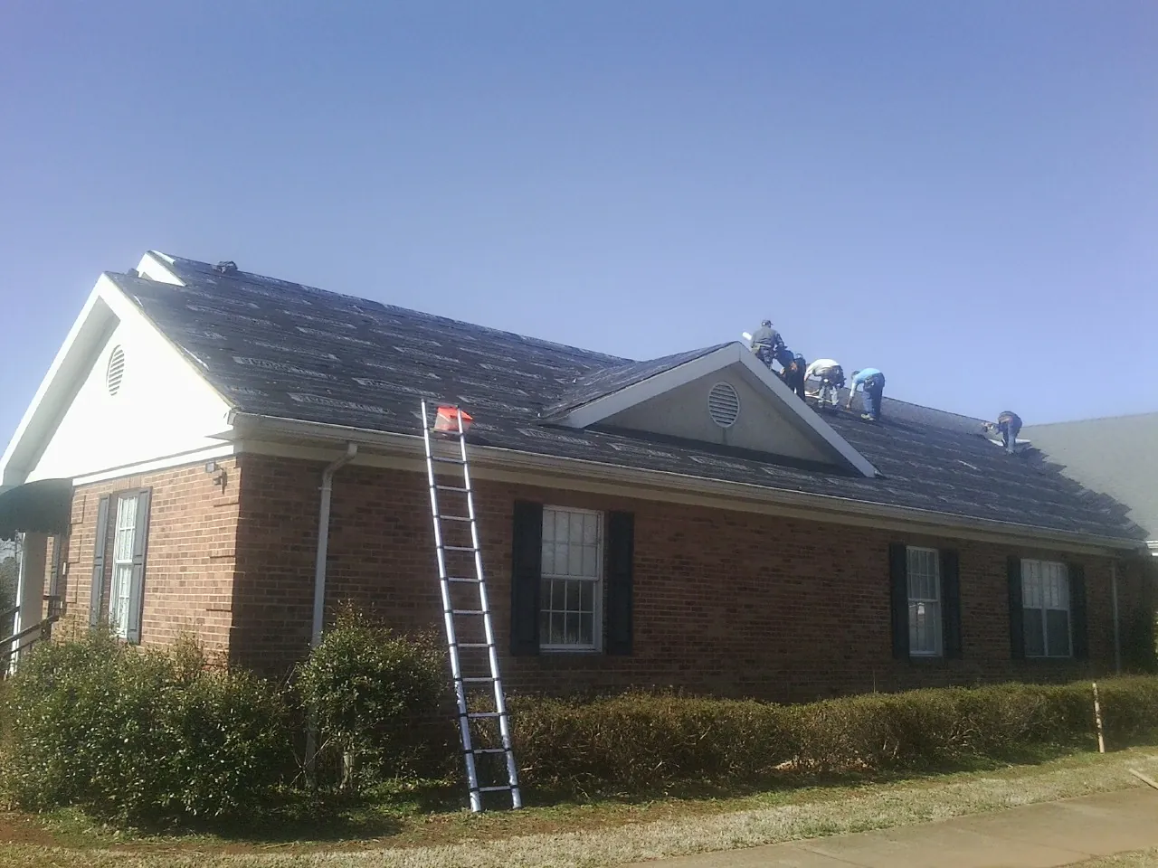 Crew tearing shingles off a brick ranch roof with a ladder set — Emergency Roof Repair work by our crew in Vanleer