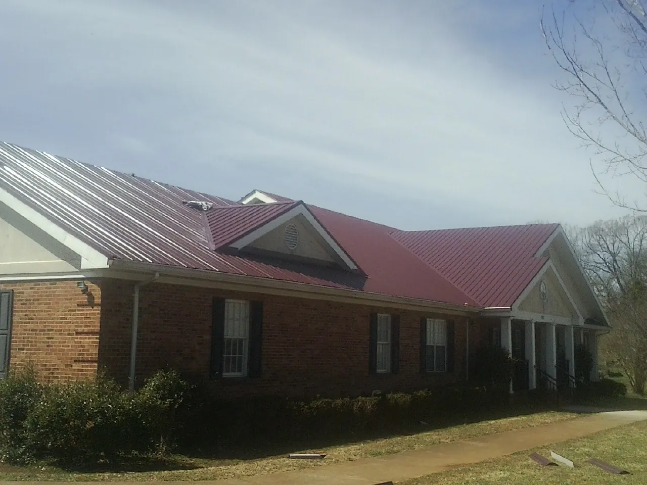Red metal roof with gabled entries on a long brick building, from a Hail Damage Roof Repair job in Vanleer
