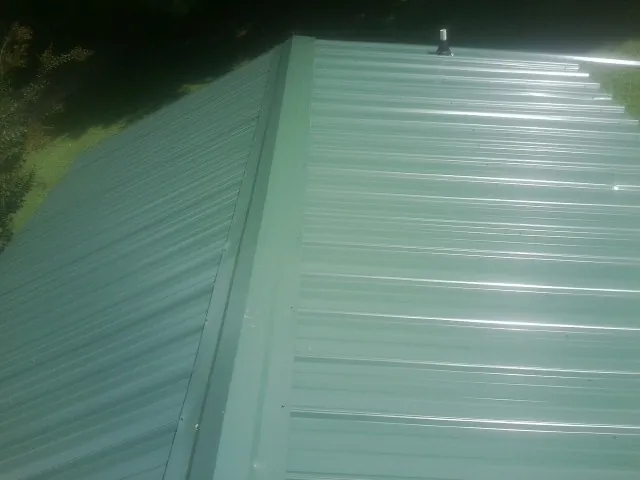 New green metal panels meeting at the ridge of a roof — Flat Roof Repair work by our crew in Vanleer