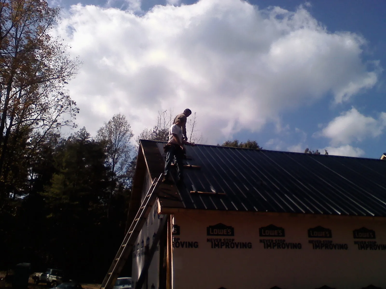 Roofer fastening dark metal panels high against a cloudy sky, from a Roof Inspection job in Vanleer