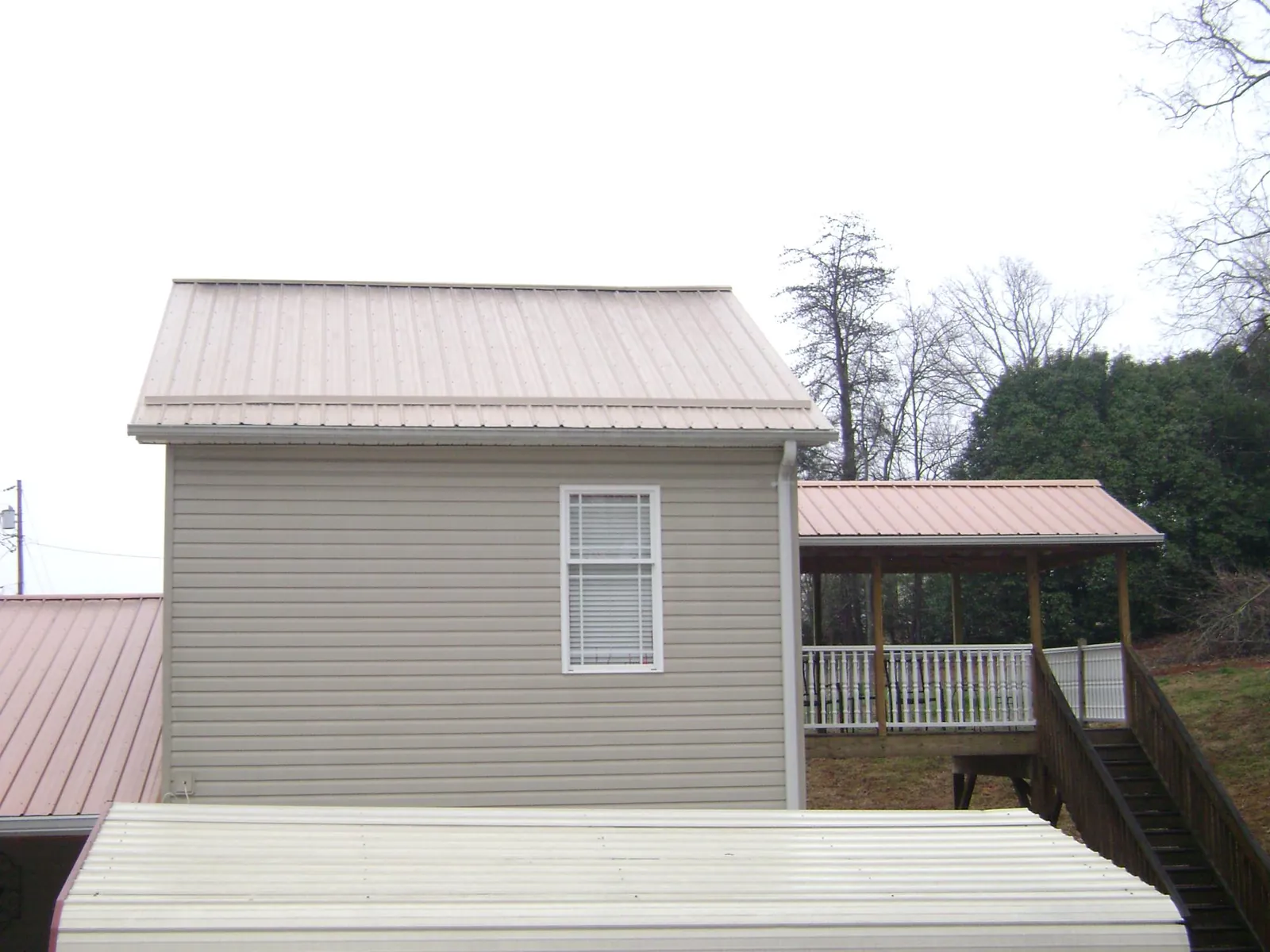 Tan metal roofs on a two story addition and attached porch, from a Roof Replacement job in Vanleer